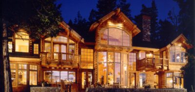 Illuminated wooden lodge with expansive arched windows.